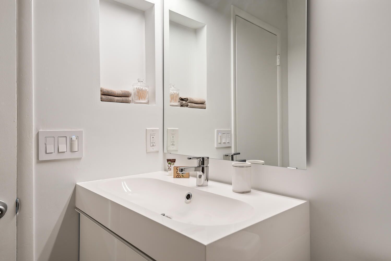Un baño moderno con un lavabo blanco, un espejo y un perchero para toallas.