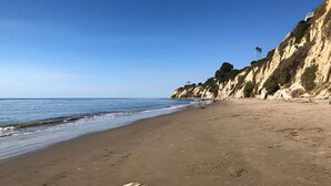 Ein Strand mit einer felsigen Klippe und blauem Himmel.