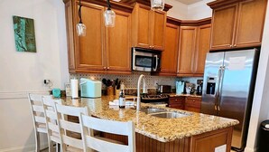 A kitchen with wooden cabinets, a granite countertop, a stainless steel refrigerator, and pendant lights. - Ocean View Townhome across from beautiful Amelia Island Beach (Fernandina Beach)