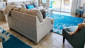 A living room with a sofa, a coffee table, a dog, and a view of the outside. - Ocean View Townhome across from beautiful Amelia Island Beach (Fernandina Beach)