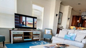 A living room with a television, a white coffee table, a blue patterned rug, and a ceiling fan. - Ocean View Townhome across from beautiful Amelia Island Beach (Fernandina Beach)