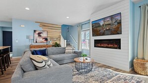 Una sala de estar moderna con un sofá seccional gris, una chimenea y un televisor grande montado en la pared.