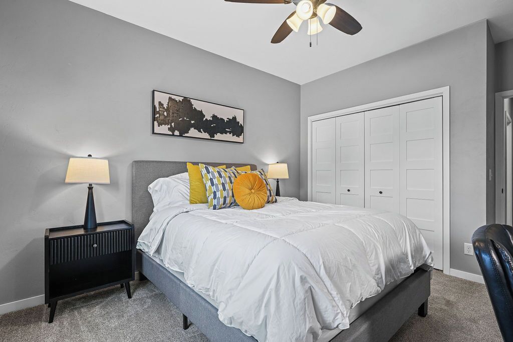 A bedroom with a bed, two bedside lamps, a ceiling fan, a door, and a wall-mounted artwork.