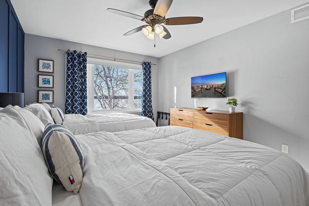 Une chambre avec deux lits, un ventilateur de plafond, une télévision et une fenêtre avec des rideaux.