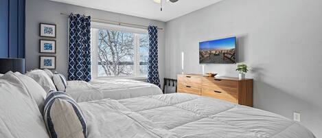 Une chambre avec deux lits, un ventilateur de plafond, une télévision et une fenêtre avec des rideaux.
