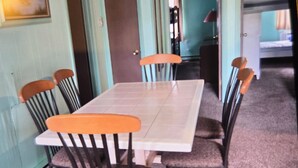 A dining area with a rectangular table surrounded by chairs, a door, and a small kitchenette in the background. - Great Location for your vacation.  Within walking distance to beach, restaurants (Ocean City)