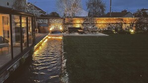 Un jardin aménagé avec un espace paysager, un point d’eau, un coin salon et un mur en pierre.