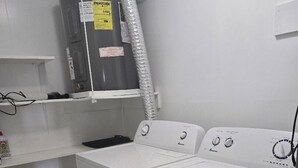 Une buanderie équipée d’un grand chauffe-eau, de deux machines à laver et d’une étagère surmontée d’une armoire blanche.