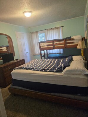 A bedroom with a bunk bed, a single bed, a dresser, a mirror, and a lamp.