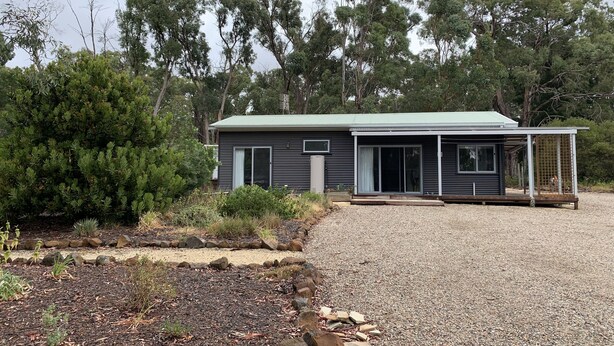 A modern two-story house with a covered patio area, surrounded by a gravel driveway and landscaped garden.