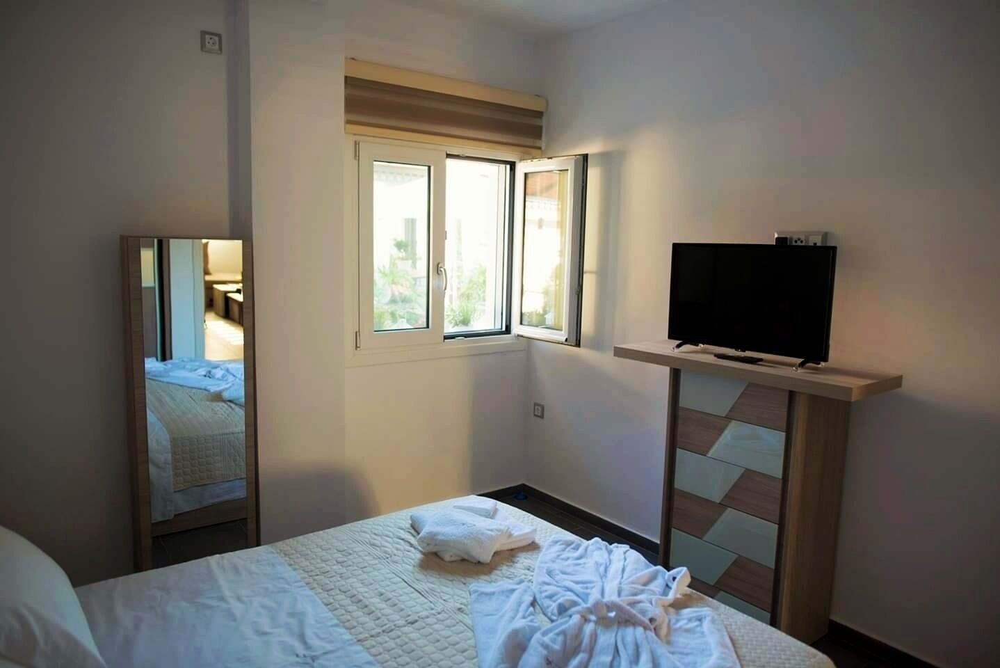 A hotel room with a bed, a television on a stand, a window with a view, and a mirror.