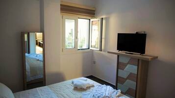 A hotel room with a bed, a television on a stand, a window with a view, and a mirror.