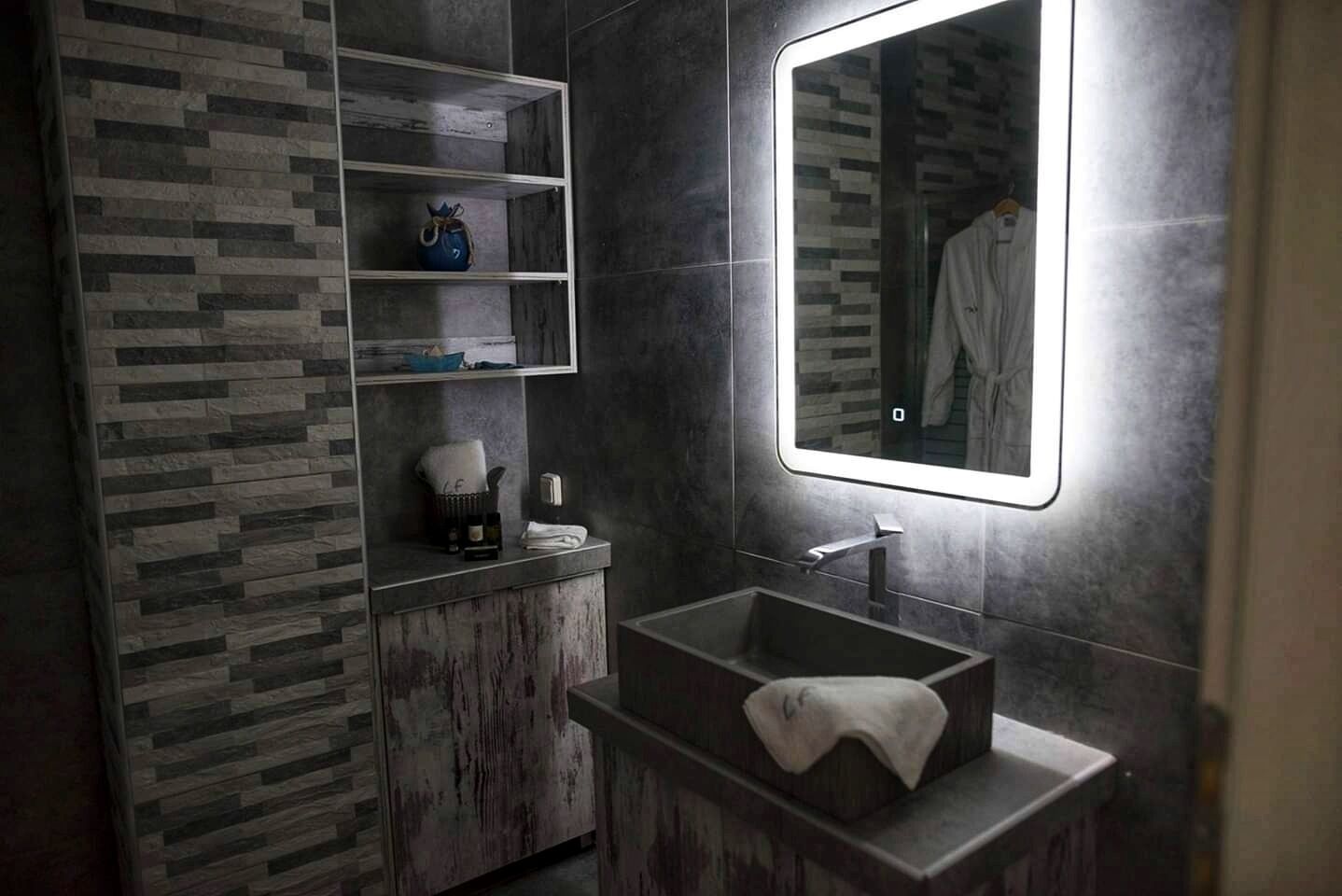 A modern bathroom with a rectangular sink, a mirror, and a shelf unit.