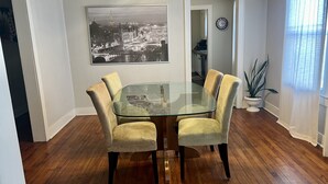 A dining area with a glass table and four chairs, a black and white cityscape painting on the wall, a clock, and a potted plant. - Home Town Getaway - 2 bed 1 bath home - close to town! (Paris)