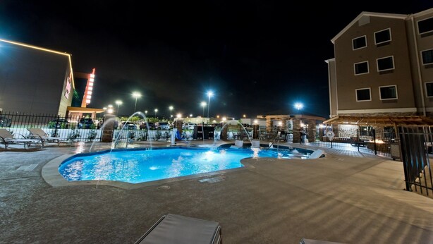 A nighttime swimming pool area with lounge chairs and a building in the background. - Accessible Studio Suite, 1 King with Tub (Humble)