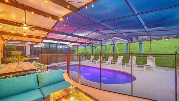 A covered outdoor area with a pool, lounge chairs, and a seating area with a table and cushions. - SALT WATER POOL*EXPANSIVE POOL DECK* LED POOL FOUNTAIN JETS (kissimmee)