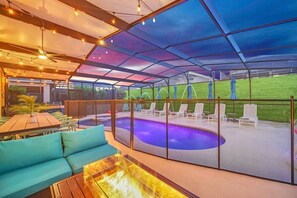 A covered outdoor area with a pool, lounge chairs, and a seating area with a table and cushions. - SALT WATER POOL*EXPANSIVE POOL DECK* LED POOL FOUNTAIN JETS (kissimmee)