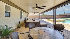 An outdoor patio with a round table and chairs, a sofa, and a ceiling fan.