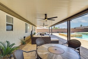 An outdoor patio with a round table and chairs, a sofa, and a ceiling fan.