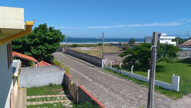 A residential street with a view of the ocean, a concrete wall, and a grassy area. - Apartment 200 meters from the beach in Imbituba, SC. (Imbituba)