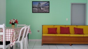 A room with a dining table set with chairs, a yellow sofa, a framed picture on the wall, and a door. - Apartment 200 meters from the beach in Imbituba, SC. (Imbituba)
