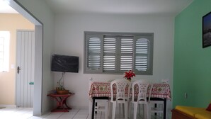 A dining area with a table set for four, a television mounted on the wall, and a window with shutters. - Apartment 200 meters from the beach in Imbituba, SC. (Imbituba)