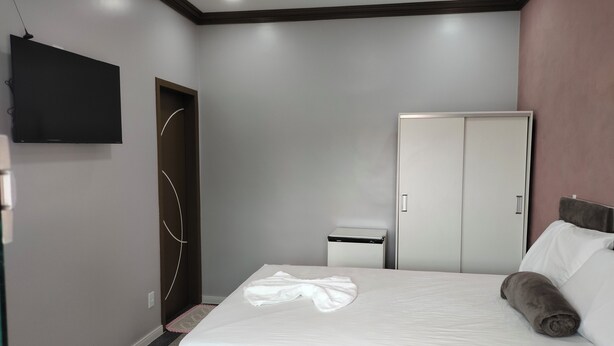 A bedroom with a bed, a wardrobe, a TV mounted on the wall, and a small bedside table.