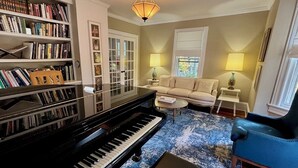 Ein Wohnzimmer mit einem Flügel, einem Bücherregal, einem Sofa und einem Couchtisch.