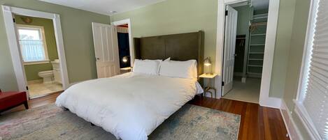 A bedroom with a large bed, a bedside table with a lamp, a red chair, and a view of a bathroom and closet.