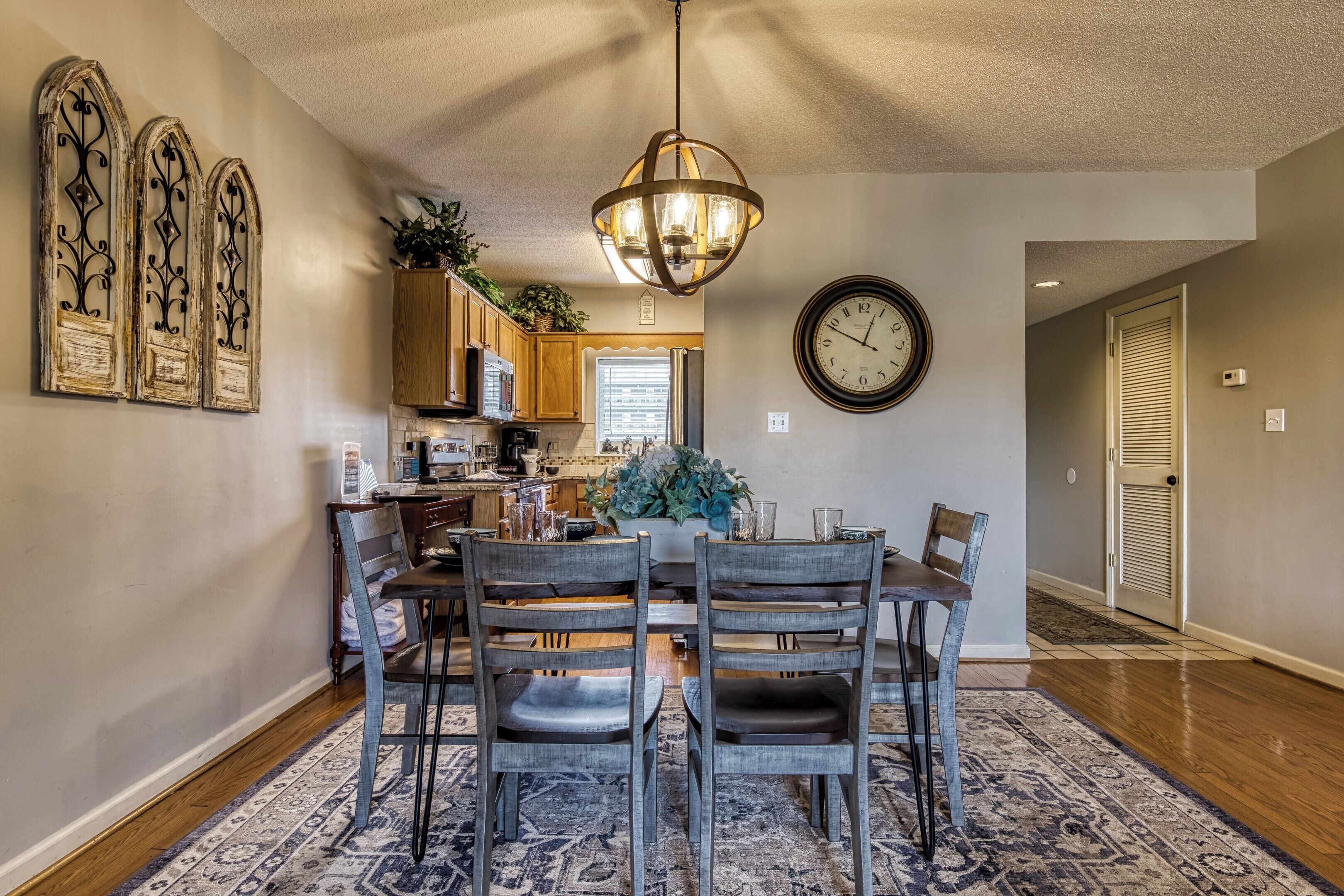A dining area with a chandelier, wooden chairs, a table, and a clock on the wall.