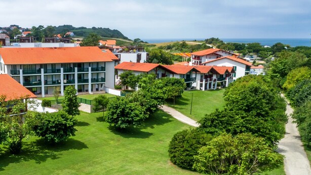 A residential area with multiple buildings, green lawns, and a clear view of the sea.
