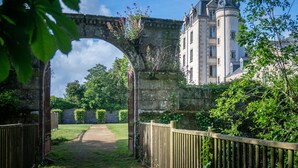 A historic building with a stone bridge, a pathway, and lush greenery.