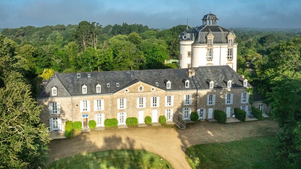 A large, historic building with multiple windows and a prominent tower, surrounded by lush greenery.