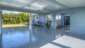 A spacious covered patio area with a concrete floor, palm trees, and a view of a golf course.