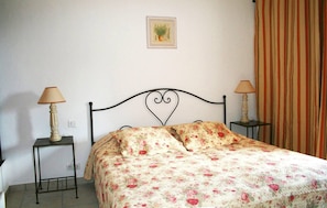 Quarto com uma cama, duas mesas de cabeceira com luminárias, uma ilustração botânica emoldurada na parede e uma cortina listrada.