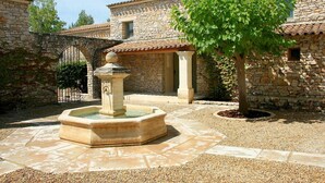 A courtyard with a stone fountain, a tree, and a stone building with a tiled roof. - Appart Duplex avec Climatisation | 2km de Gordes (Gordes)