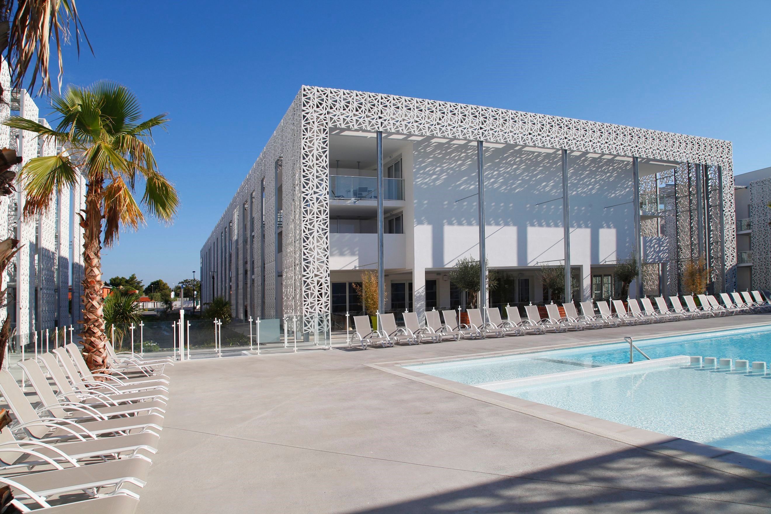 Een modern hotel met een zwembad, ligbedden en palmbomen.