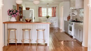 Una cocina con una isla de madera, taburetes de bar, un refrigerador y un comedor con una silla y mesa.