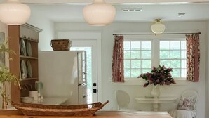 Una cocina con isla central, taburetes de bar, una ventana con cortinas y una mesa de comedor con sillas.