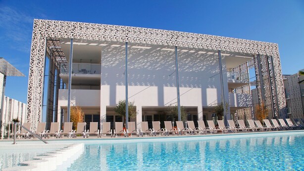 A modern hotel with a pool, sun loungers, and a geometric facade. - Studio 150m de la Plage | Sauna + Accès Piscine (Cap d'Agde)