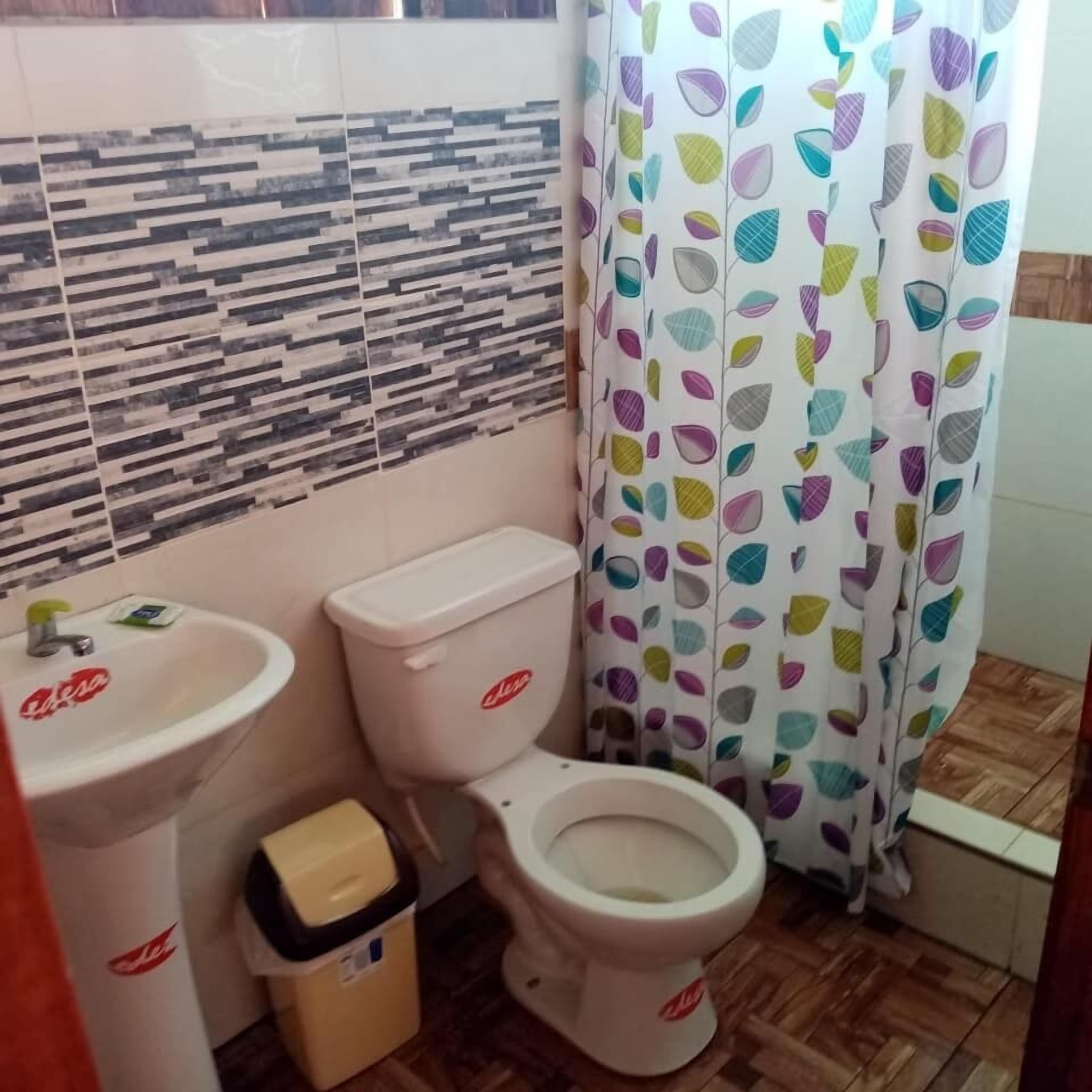 Un baño con inodoro, lavamanos y un cubo de basura.