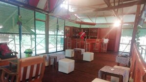 A spacious room with wooden flooring, white cushioned seating, a bar area, and large windows. - Amazon Journeys Lodge & Expedition (Indiana)