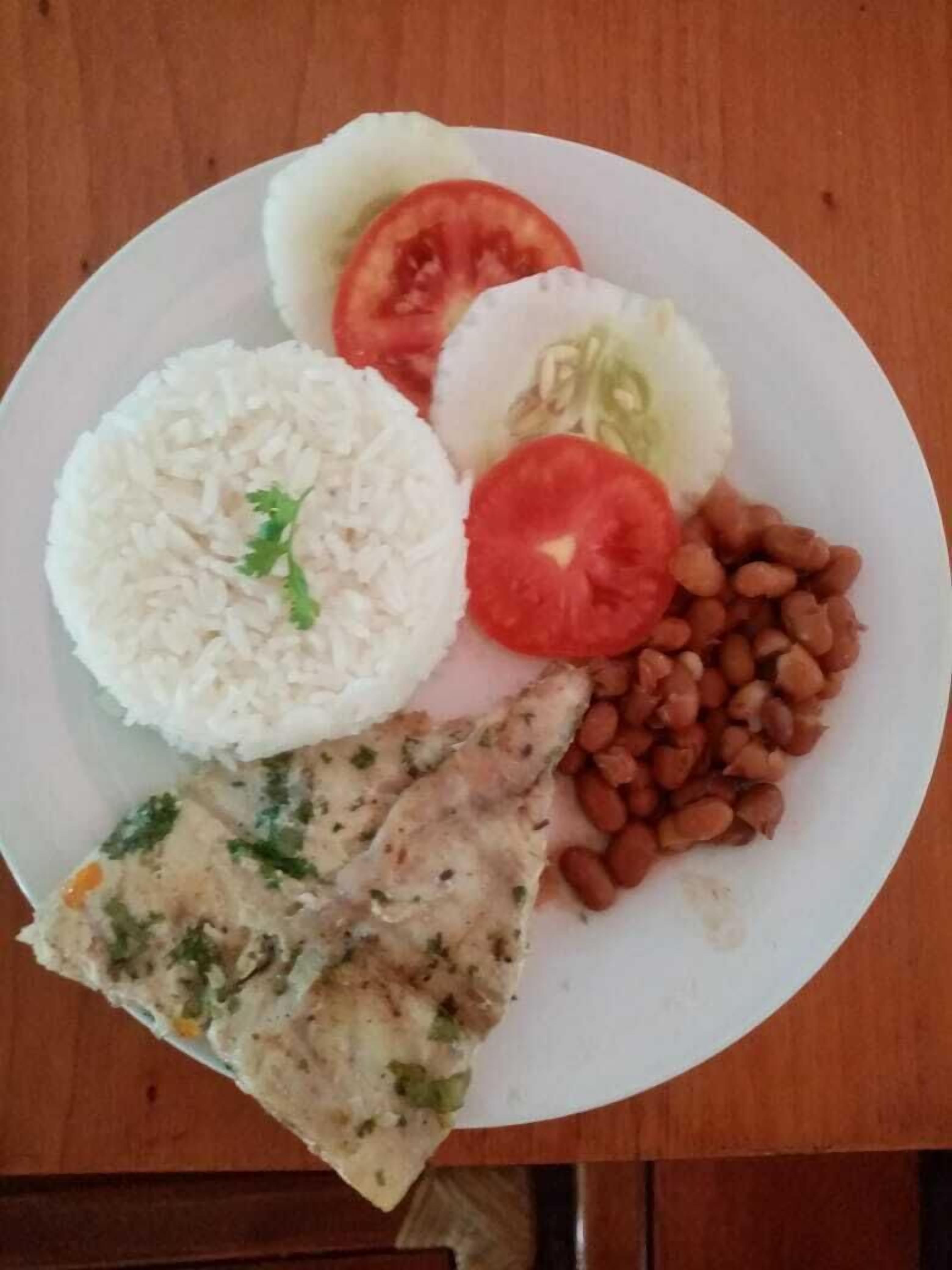 Une assiette de riz blanc, de tomates en tranches, de concombres et de haricots.