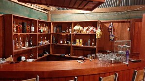 A bar area with wooden shelves stocked with bottles and glasses, a counter with a glass display, and bar stools. - Amazon Journeys Lodge & Expedition (Indiana)