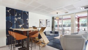 A modern interior with a dining area, bar stools, a sofa, and a large abstract painting on the wall. - Studio Climatisé | 10 Minutes de la Plage! (Cavalaire-sur-Mer)