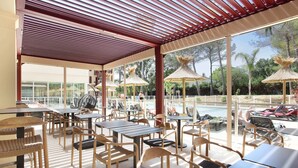 An outdoor seating area with tables and chairs, large umbrellas, and a view of a swimming pool. - Studio Climatisé | 10 Minutes de la Plage! (Cavalaire-sur-Mer)