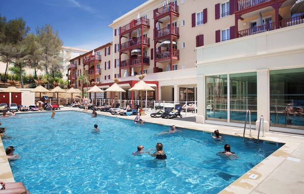 Ein Poolbereich mit mehreren Balkonebenen, Sonnenschirmen und Liegestühlen.