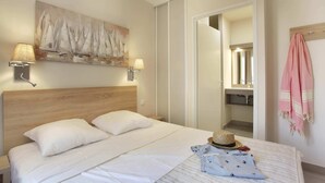 Ein ordentlich bezogenes Bett mit weißen Leinen, einem Holz-Kopfteil und einem Gemälde von Segelbooten an der Wand.