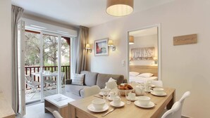 Habitación de hotel moderna con zona de comedor, sofá y balcón con mobiliario exterior.