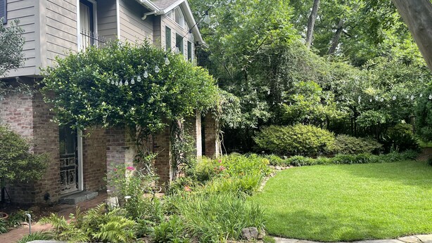 A house with a brick exterior, a stone pathway, and a well-maintained garden with various plants and a lawn.